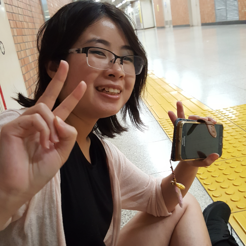 Photo of Sarah sitting in Shinjuku-sanchome train station, making the victory sign with two hands